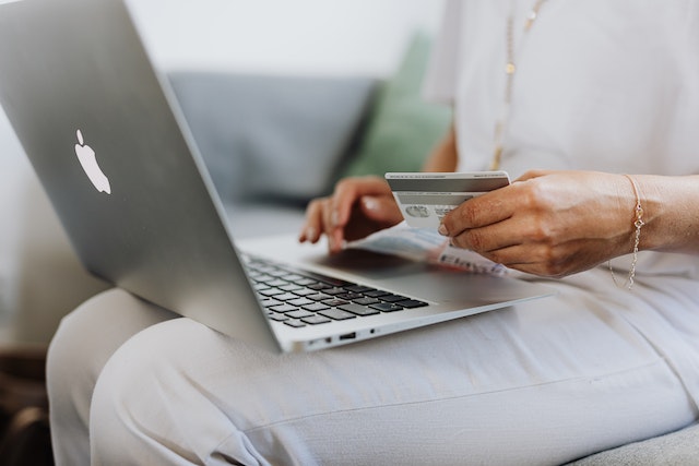 A woman holding her credit card and typing on a Macbook laptop to shop on eBay